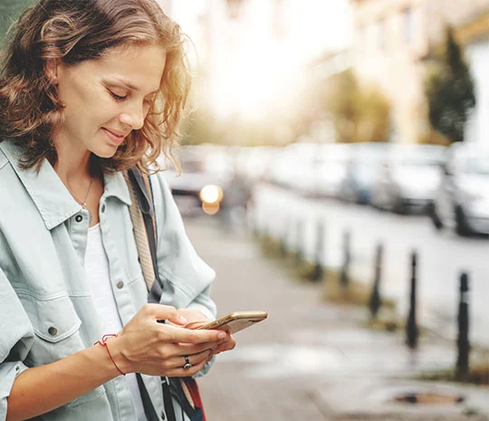 Kvinna står på trottoar med mobilen
