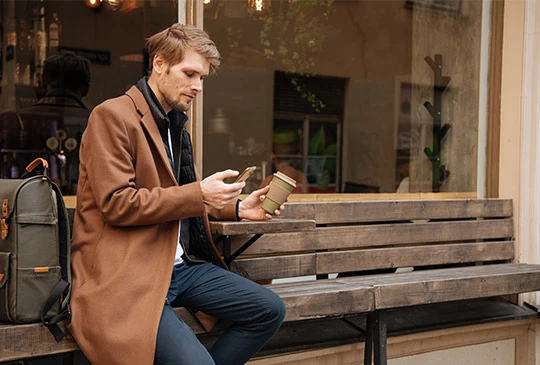 Man dricker kaffe och jämför lån i mobilen